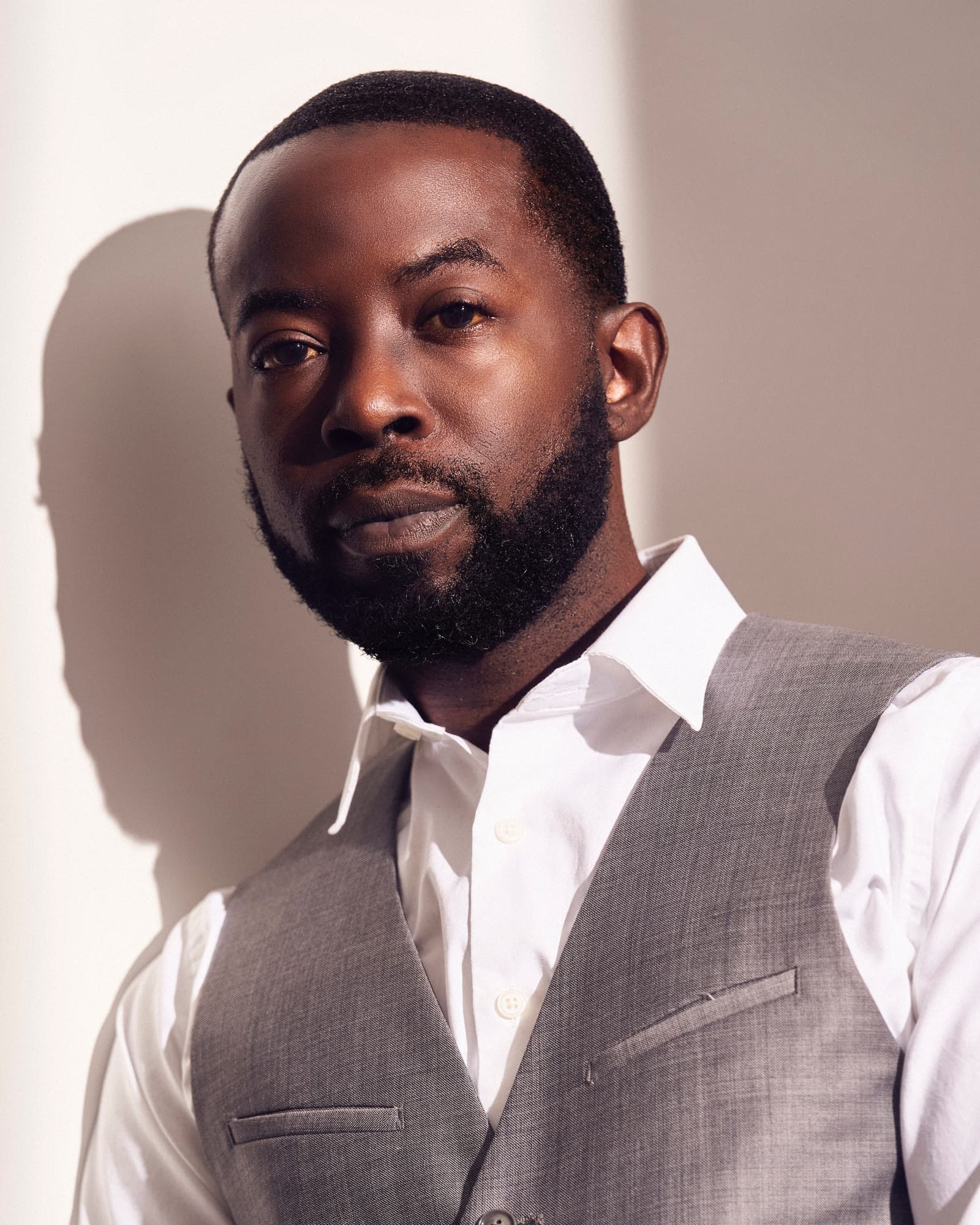 Charlie Hudson III in a white shirt and grey waistcoat, lit by warm directional light against a pale wall.